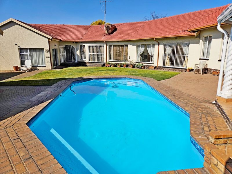 A spacious rear garden featuring a swimming pool with brick paving, surrounded by the main house structure with a tiled roof.