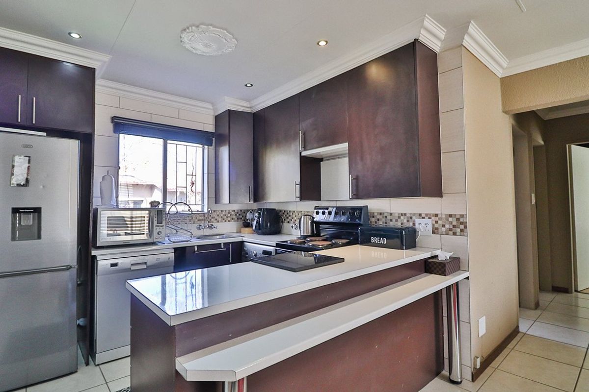 A functional kitchen featuring dark wood-finish cabinetry, a breakfast bar, tiled backsplash, and tiled flooring, offering a practical layout for daily use.