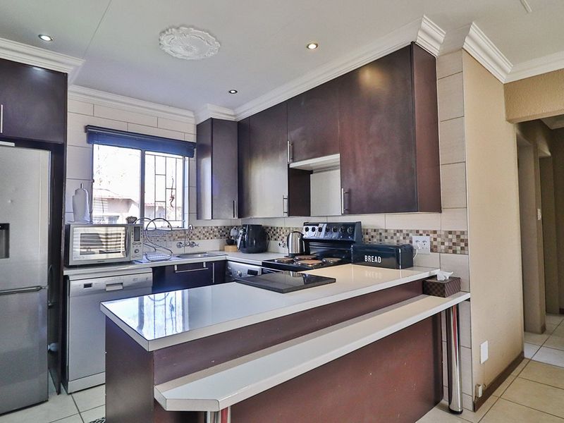 A functional kitchen featuring dark wood-finish cabinetry, a breakfast bar, tiled backsplash, and tiled flooring, offering a practical layout for daily use.