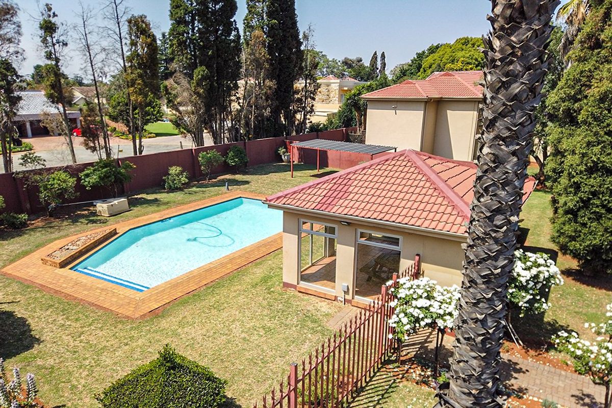 Aerial view of a residential backyard featuring a swimming pool, landscaped garden, and a detached outbuilding with a tiled roof.