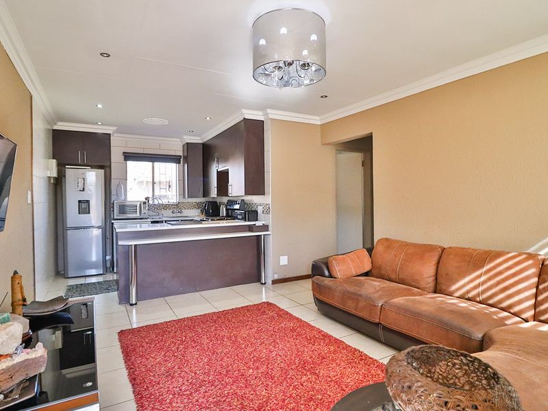 Open-plan living area featuring a functional kitchen with breakfast bar, tiled flooring, and neutral wall tones, creating a cohesive and practical living space.