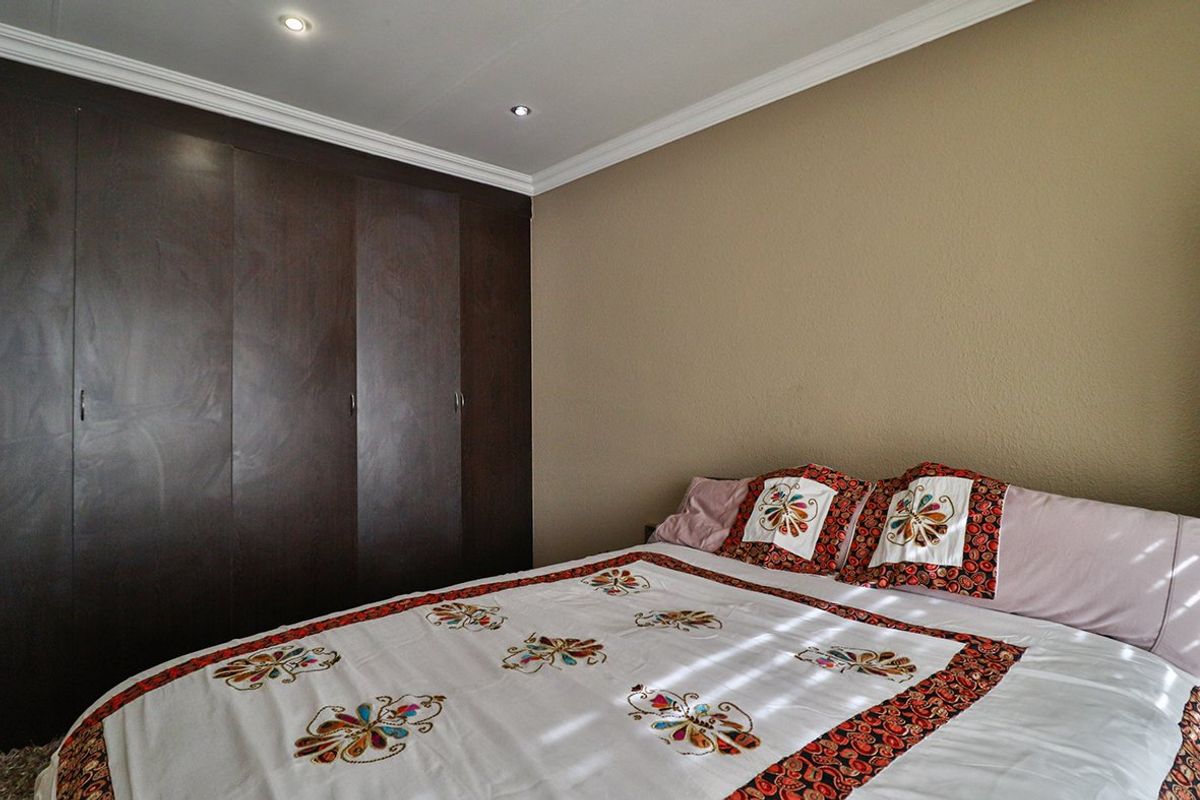 A well-maintained bedroom featuring dark wood built-in cupboards, recessed downlighting, and decorative ceiling cornicing.