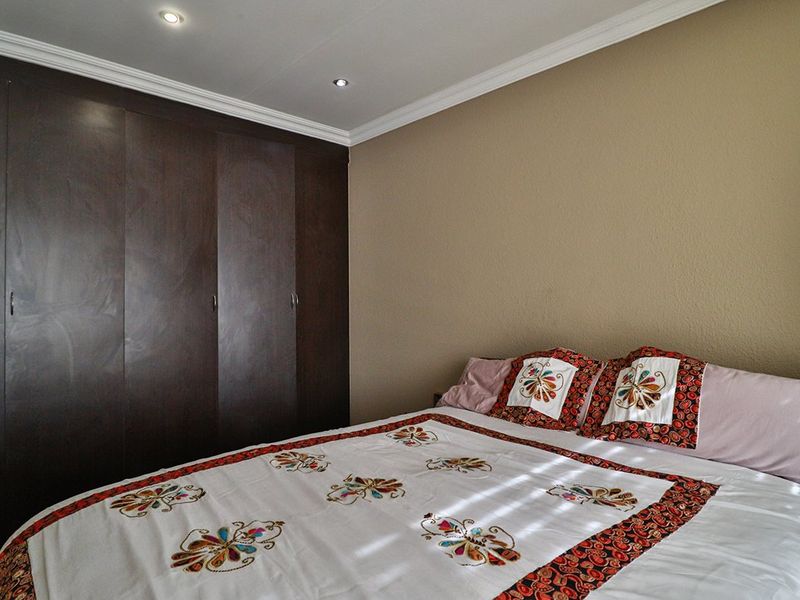 A well-maintained bedroom featuring dark wood built-in cupboards, recessed downlighting, and decorative ceiling cornicing.