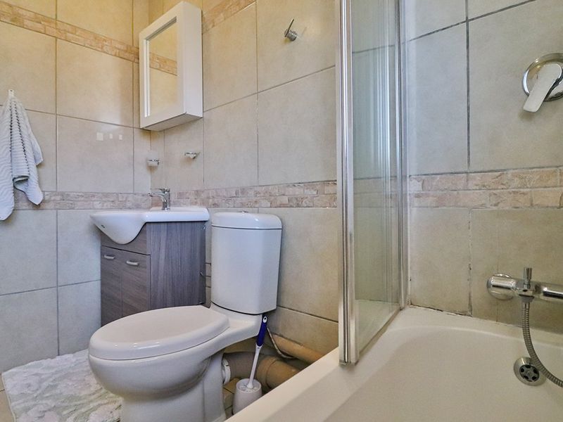 A functional bathroom featuring a vanity cabinet, toilet, and a bathtub with a glass shower screen, finished with neutral wall tiling.