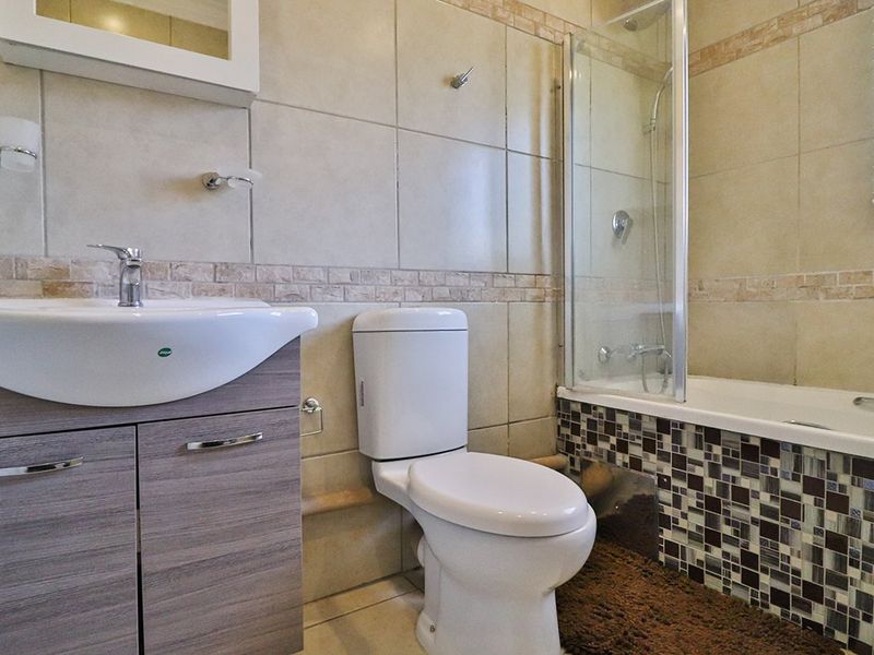 A functional bathroom featuring a vanity with basin, toilet, and a bathtub with a glass shower screen and decorative mosaic tile detailing.