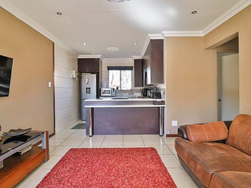 Open-plan living area featuring a functional kitchen with built-in cabinetry, a breakfast bar, and tiled flooring throughout the combined space.