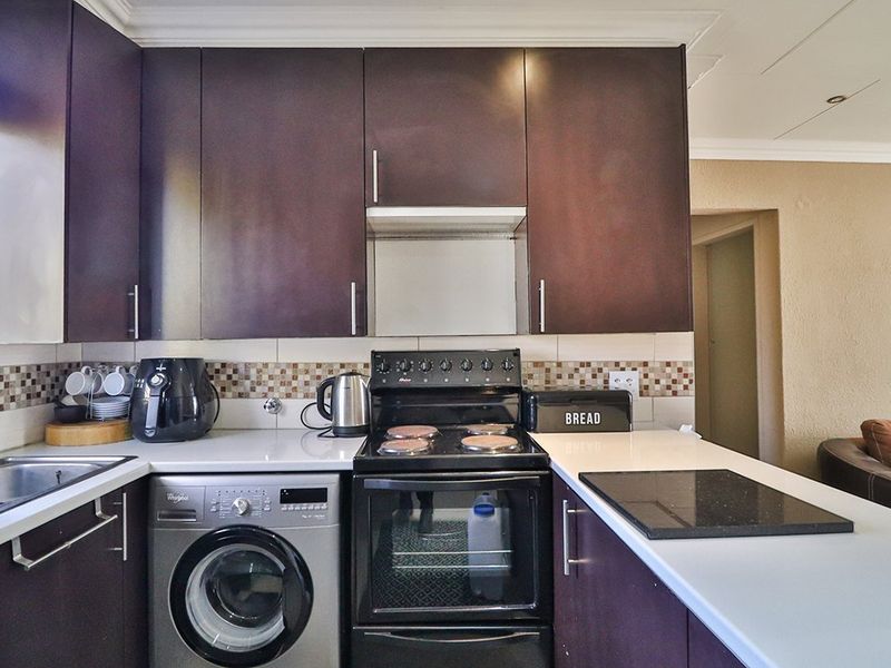 Compact kitchen featuring dark wood cabinetry, mosaic tile backsplash, integrated washing machine, and built-in oven with electric stove.