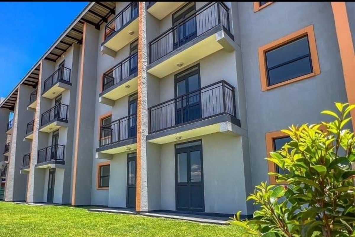 Exterior view of a modern apartment building featuring multiple levels of balconies with metal railings and well-maintained surrounding lawn.
