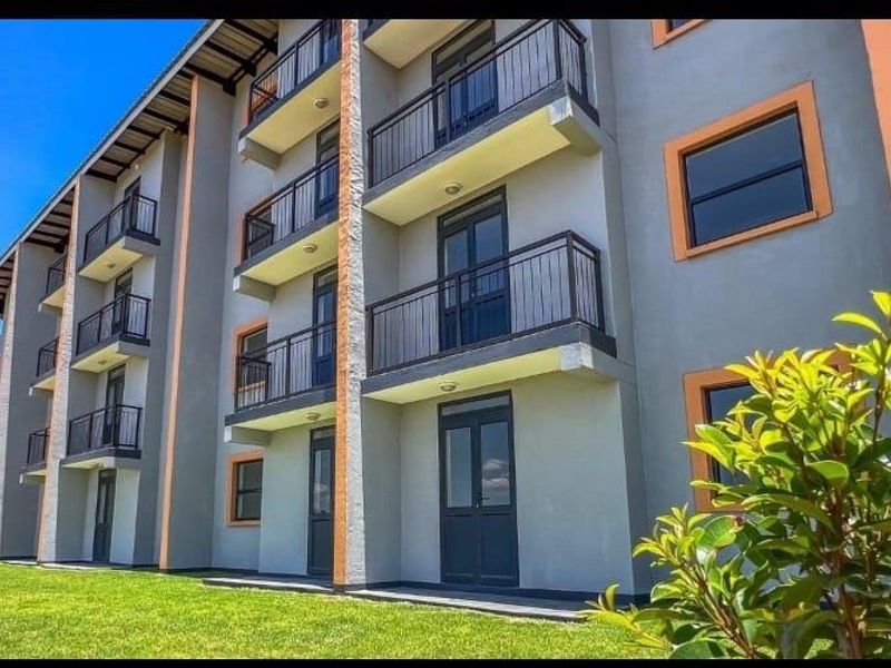 Exterior view of a modern apartment building featuring multiple levels of balconies with metal railings and well-maintained surrounding lawn.