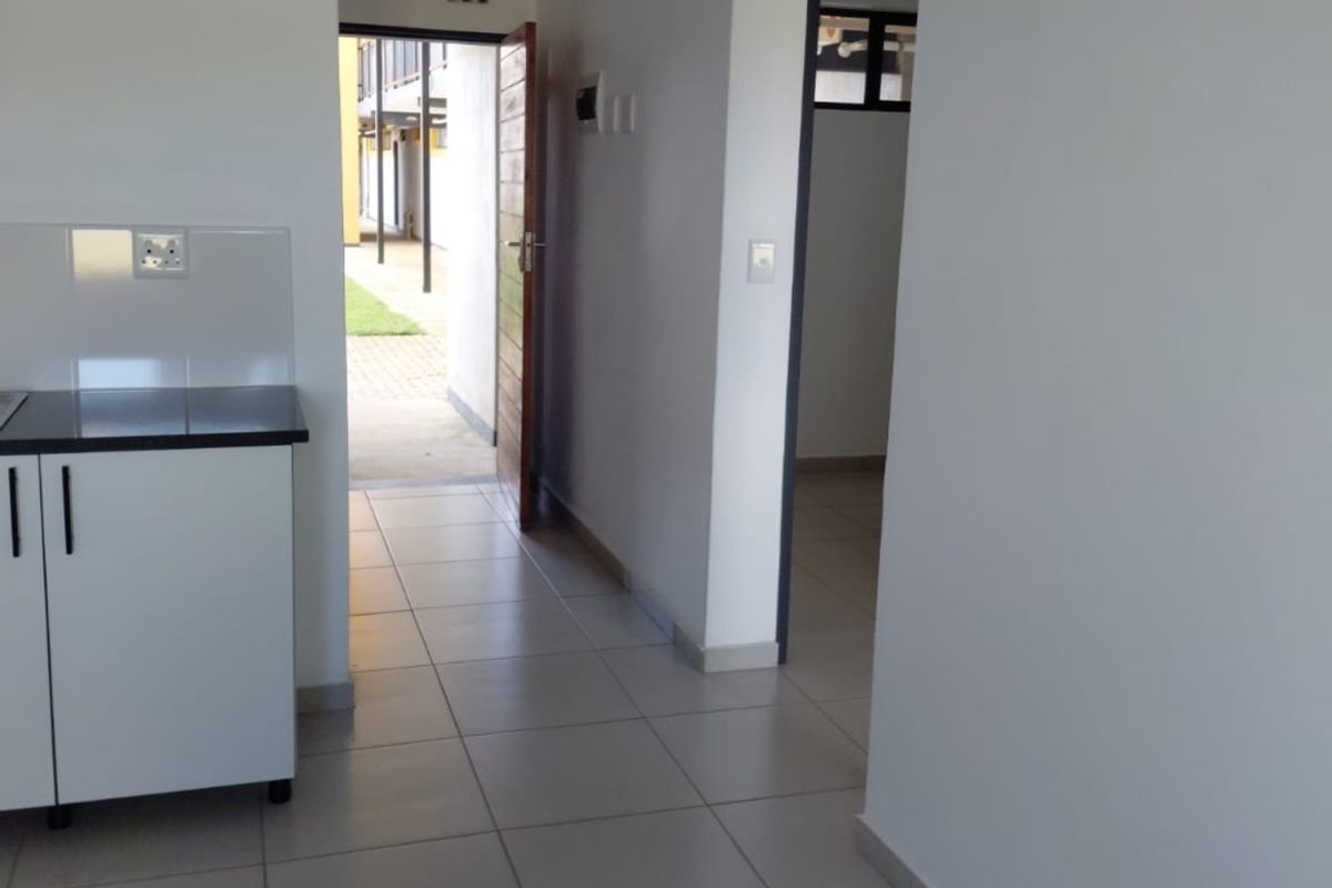 A clean, empty kitchen area featuring tiled flooring, white cabinetry with dark countertops, and direct access to the exterior entrance.
