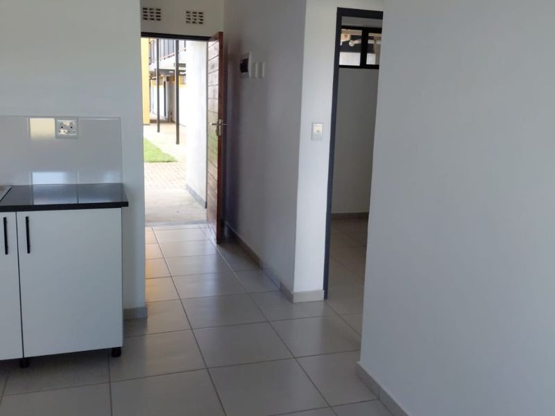 A clean, empty kitchen area featuring tiled flooring, white cabinetry with dark countertops, and direct access to the exterior entrance.