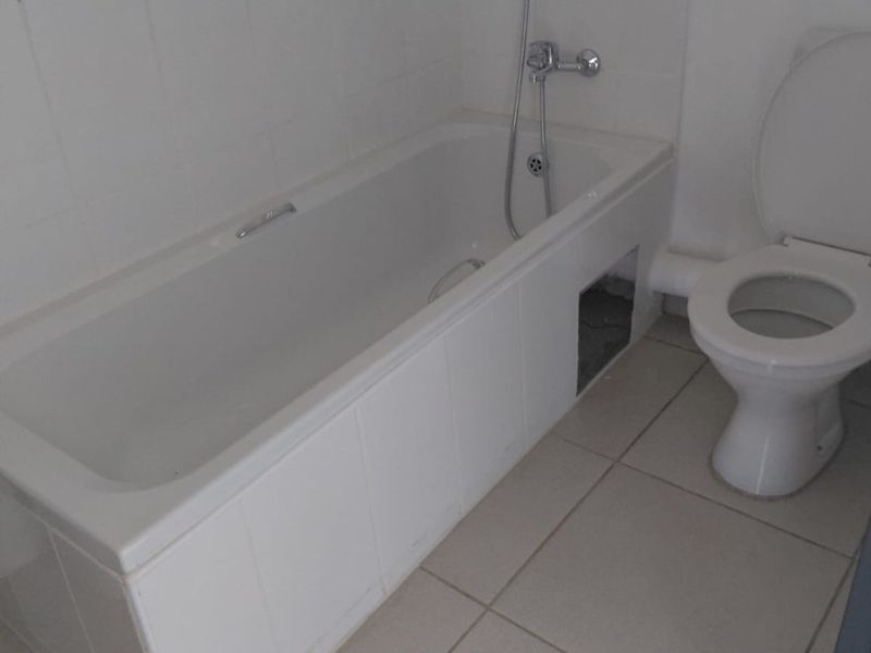 A functional bathroom featuring a bathtub with a handheld shower attachment and a standard toilet, finished with neutral wall and floor tiles.