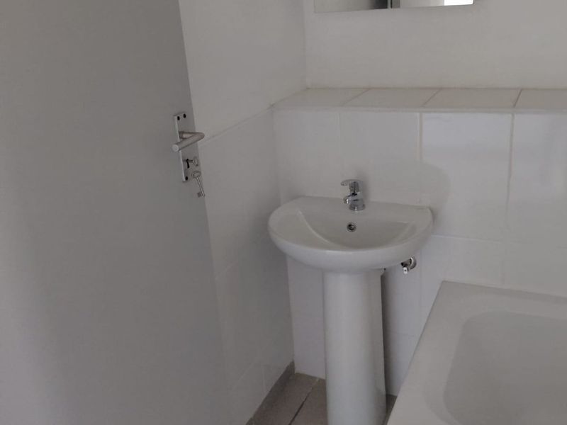 A functional bathroom featuring a pedestal basin, chrome fixtures, a built-in bathtub, and a wall-mounted medicine cabinet with neutral tiled finishes.