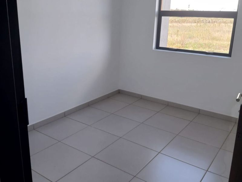 A clean, empty bedroom featuring neutral floor tiles and a large window with an aluminium frame, offering a bright and versatile living space.