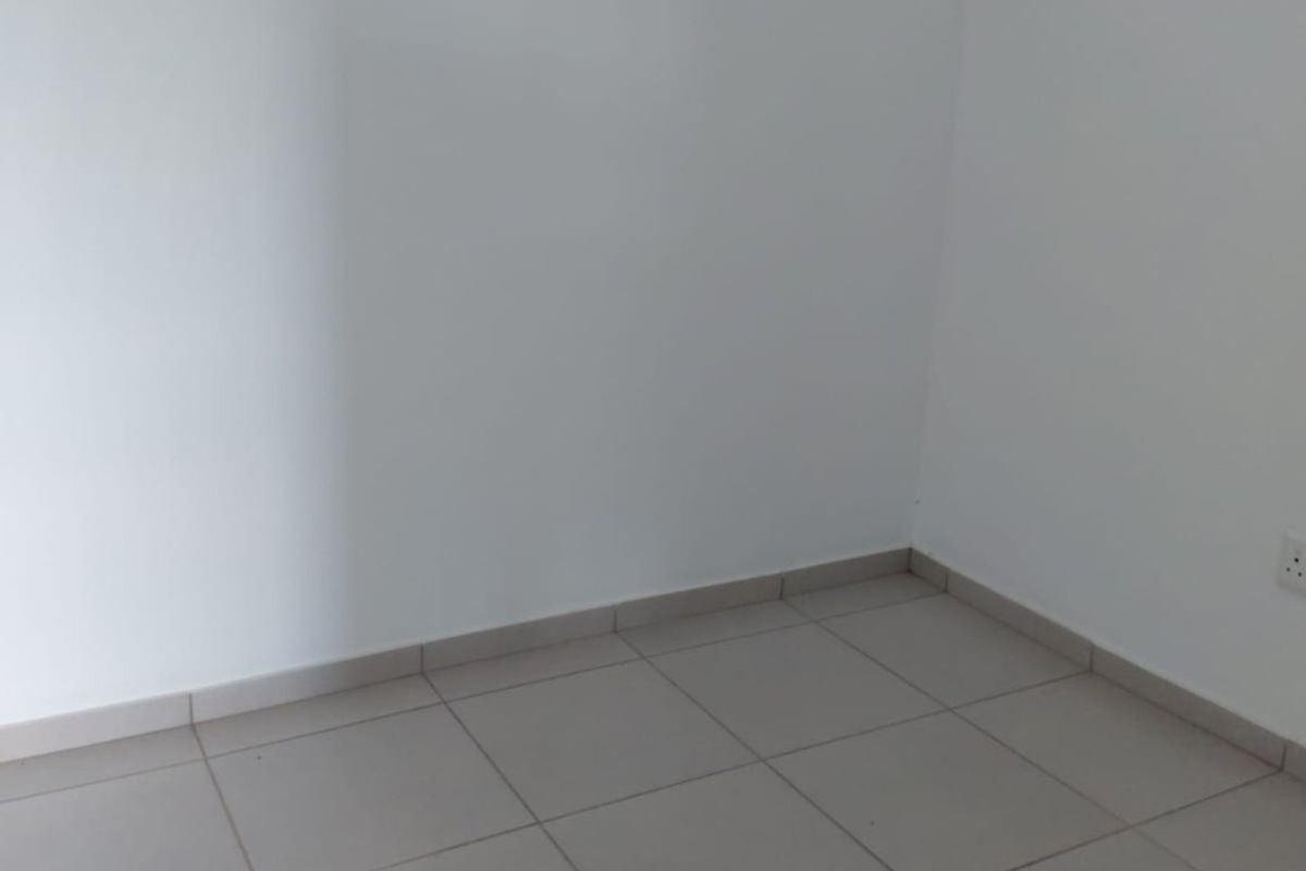 A clean, empty bedroom featuring neutral tiled flooring, white walls, and a high-level window providing natural light.