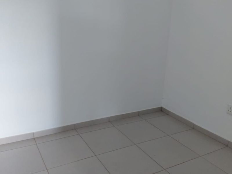 A clean, empty bedroom featuring neutral tiled flooring, white walls, and a high-level window providing natural light.