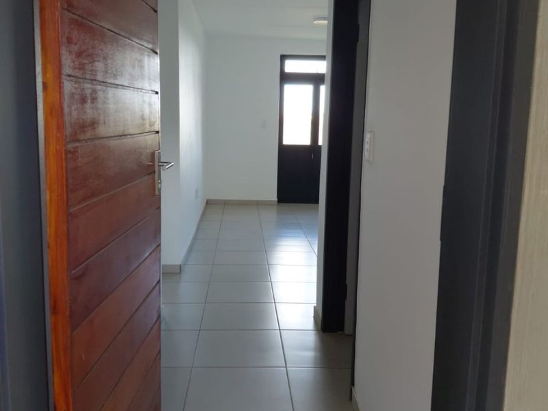 A clean, empty hallway featuring neutral tiled flooring and a timber door, providing access to other areas of the apartment.