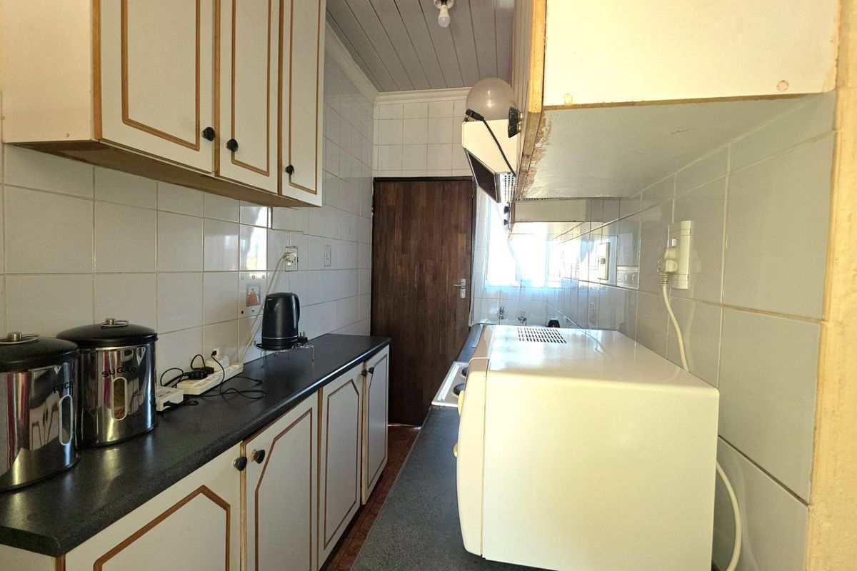 A compact galley-style kitchen featuring tiled walls, laminate countertops, and traditional built-in cabinetry, offering a functional layout with potential for modern updates.