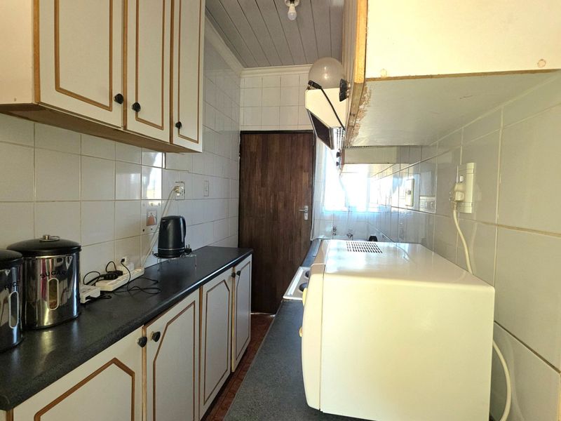 A compact galley-style kitchen featuring tiled walls, laminate countertops, and traditional built-in cabinetry, offering a functional layout with potential for modern updates.
