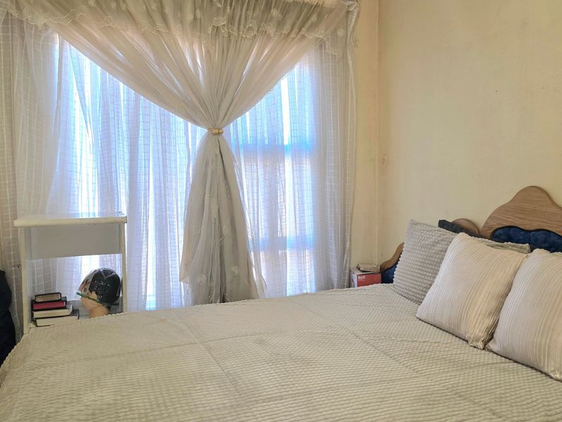 A bedroom featuring a window with curtains and plain wall finishes, requiring cosmetic updates to improve the overall aesthetic.