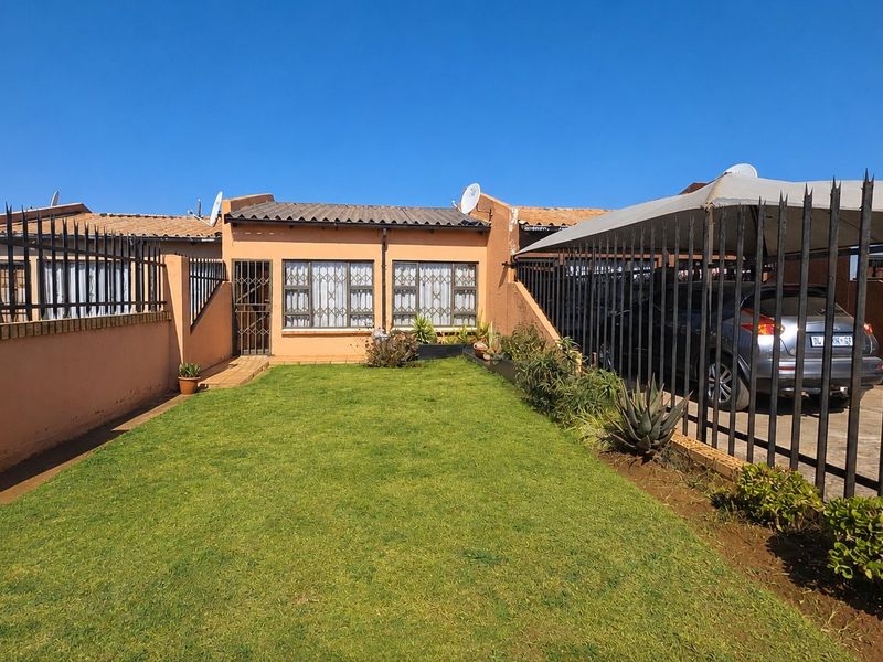Front view of the property featuring a lawn, carport, and secure perimeter fencing with security bars on windows.