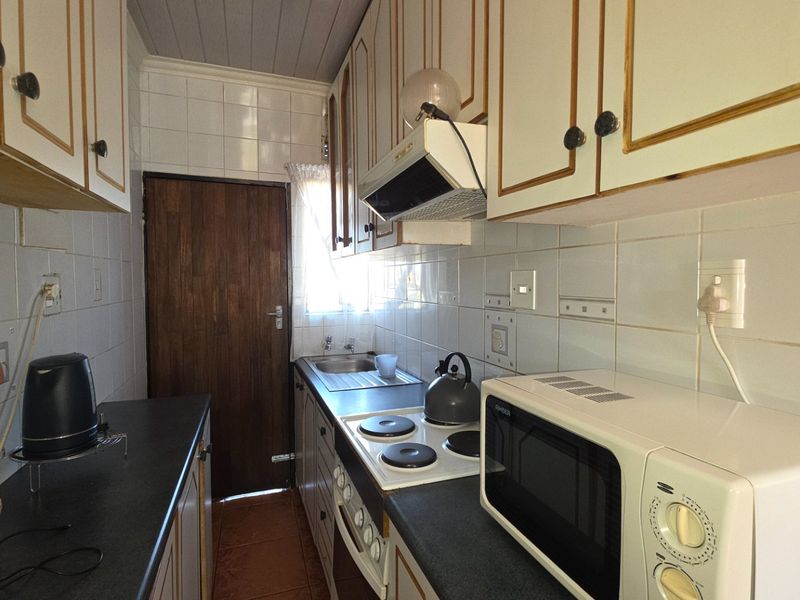 A compact, functional kitchen featuring dated cabinetry, tiled backsplash, built-in electric hob, oven, and extractor fan with a rear door access.