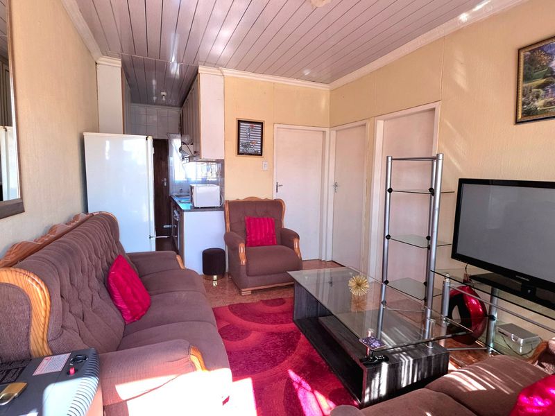 Open plan living area featuring tiled flooring, panelled ceiling, and an integrated kitchen space with cabinetry.