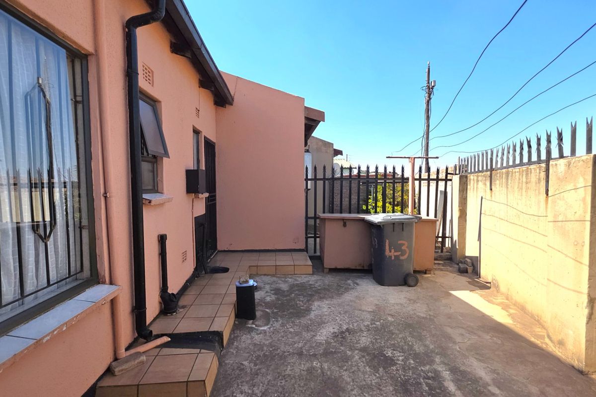 Rear exterior area featuring a tiled patio, perimeter wall with security spikes, and access to the main dwelling via a security gate.