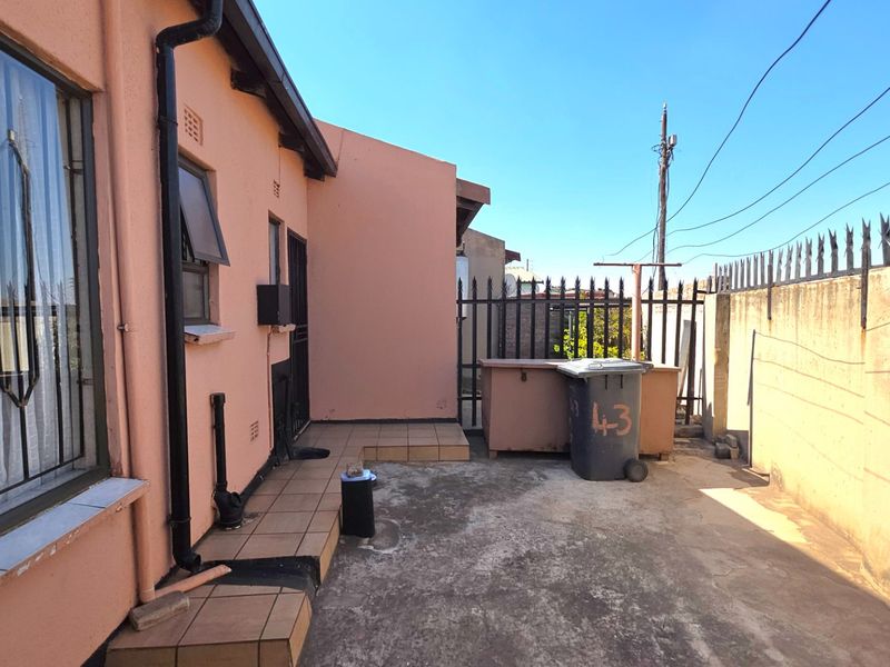 Rear exterior area featuring a tiled patio, perimeter wall with security spikes, and access to the main dwelling via a security gate.