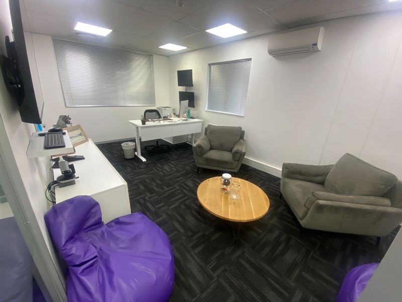 A functional commercial office space featuring carpeted flooring, recessed ceiling lighting, and a wall-mounted split-system air conditioning unit.