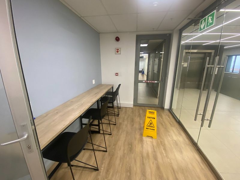 A modern commercial hallway featuring a built-in wooden desk, glass partitioning, and professional finishes, providing a clean and functional transition space.