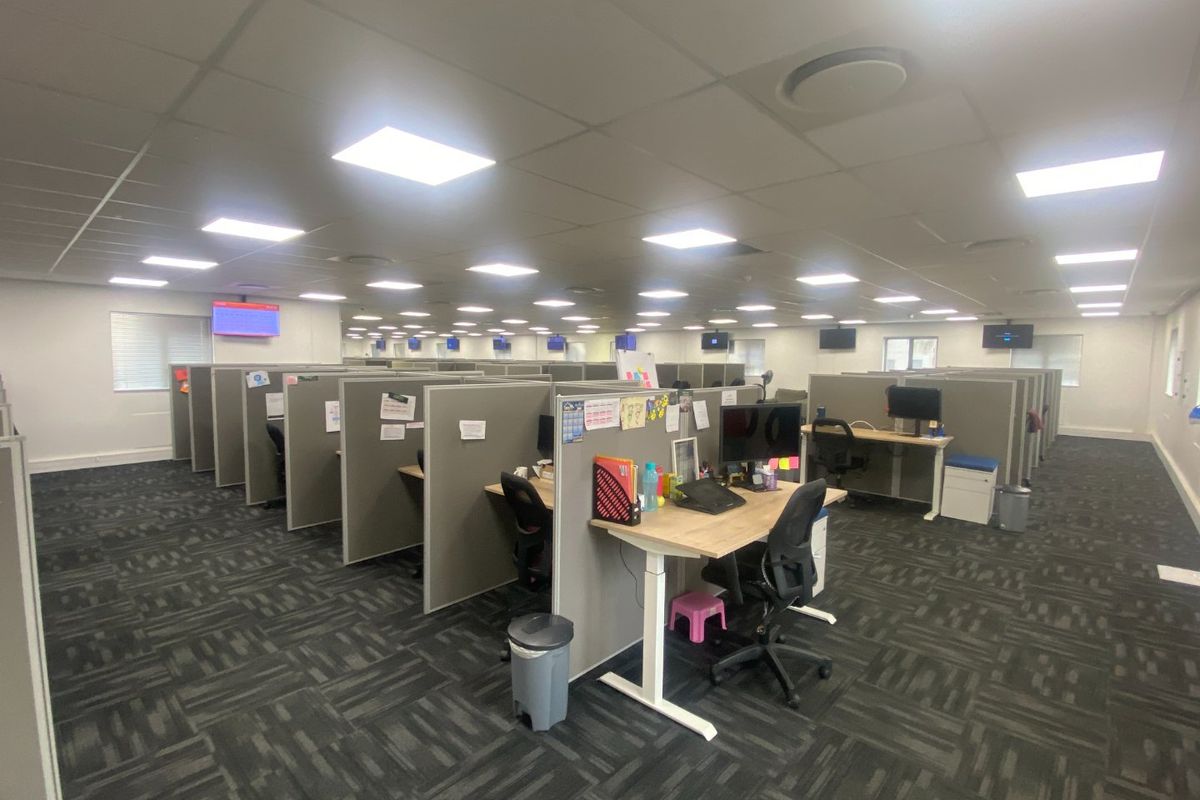 Spacious open-plan commercial office area featuring modular cubicle workstations, suspended ceilings with recessed lighting, and durable carpet tile flooring.