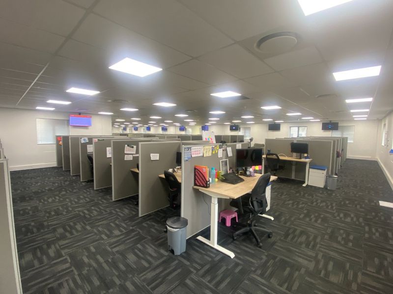 Spacious open-plan commercial office area featuring modular cubicle workstations, suspended ceilings with recessed lighting, and durable carpet tile flooring.