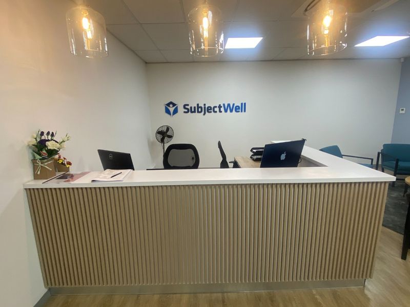 A professional commercial reception area featuring a modern slatted timber desk, recessed ceiling lighting, and contemporary pendant fixtures.
