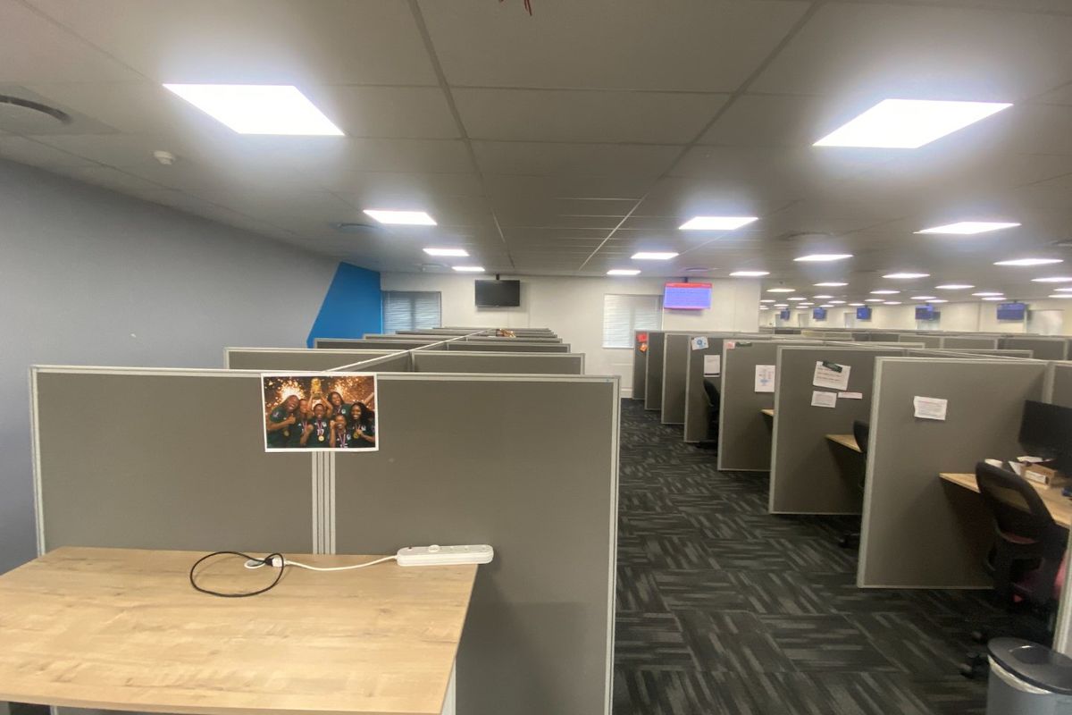 A large open-plan commercial office space featuring rows of modular cubicle workstations, suspended ceiling tiles, and recessed lighting.