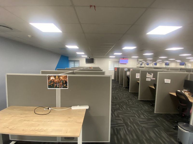 A large open-plan commercial office space featuring rows of modular cubicle workstations, suspended ceiling tiles, and recessed lighting.
