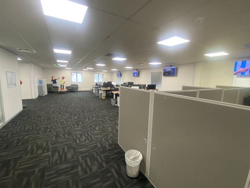 Open-plan commercial office space featuring modular cubicle partitions, suspended ceilings with recessed lighting, and carpeted flooring.