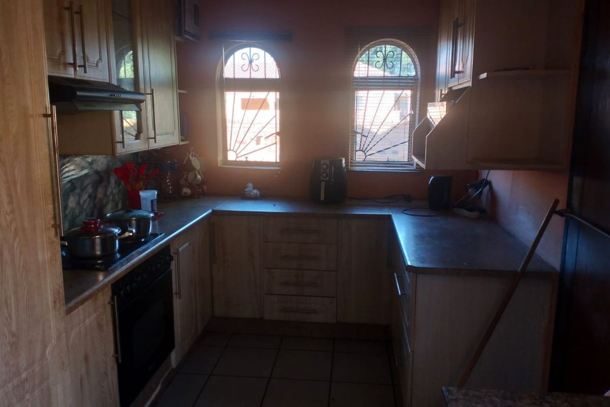 A functional U-shaped kitchen featuring wood-finish cabinetry, laminate countertops, built-in oven and hob, and arched windows with security bars.