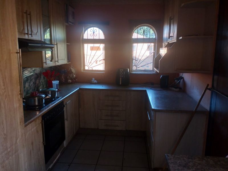 A functional U-shaped kitchen featuring wood-finish cabinetry, laminate countertops, built-in oven and hob, and arched windows with security bars.