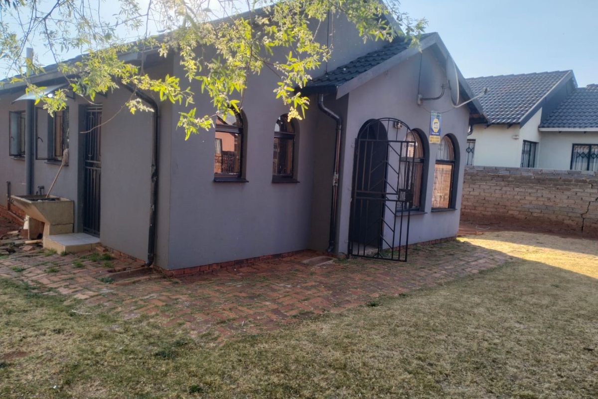 Rear view of the house featuring arched windows, security gates, brick paved patio area, and an external wash basin.