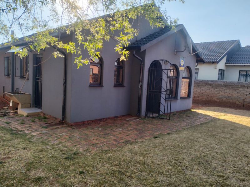 Rear view of the house featuring arched windows, security gates, brick paved patio area, and an external wash basin.