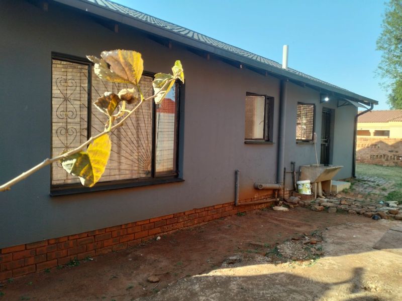 Rear exterior view of the house featuring dark grey painted walls, security bars on windows, and an external utility wash basin.