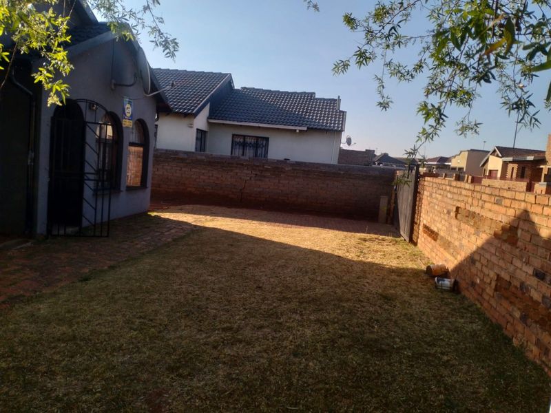 A rear garden area featuring a paved walkway, brick boundary walls, and a security gate, showing standard residential maintenance.