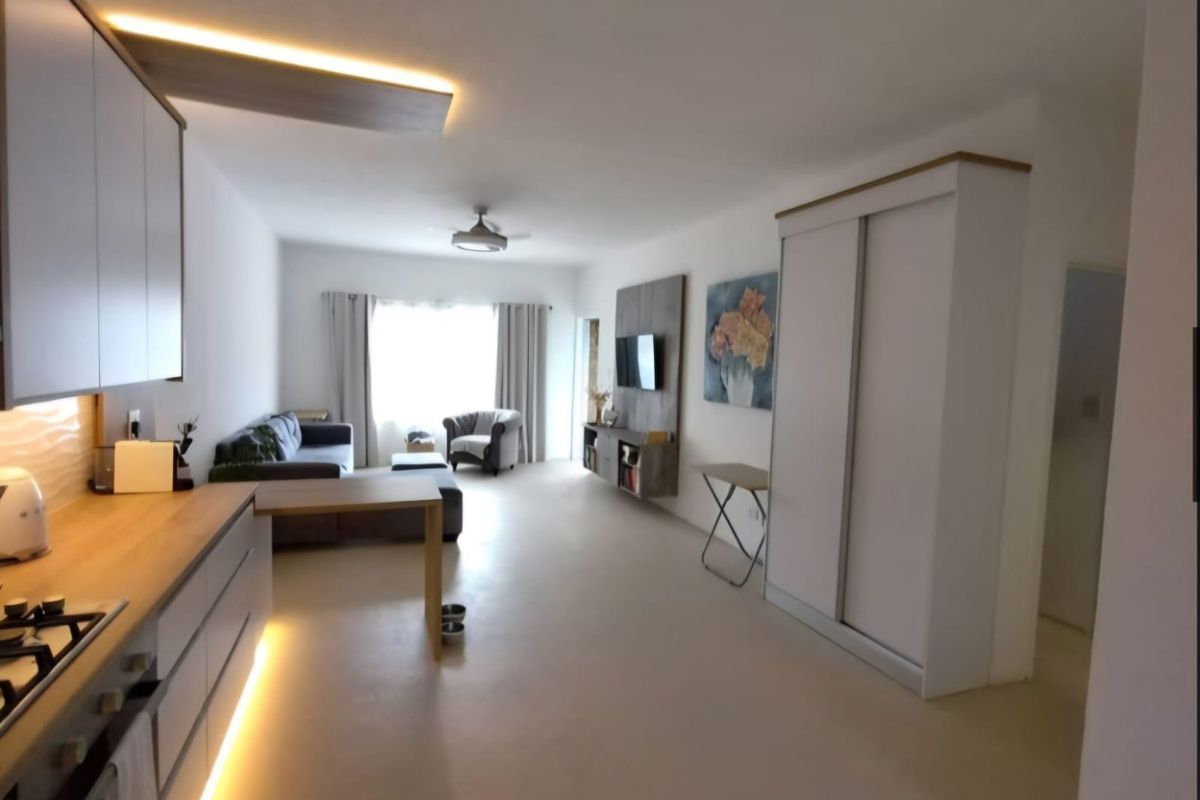 Modern open-plan living area featuring a sleek kitchen with under-cabinet lighting, integrated gas hob, and a spacious built-in wardrobe for storage.