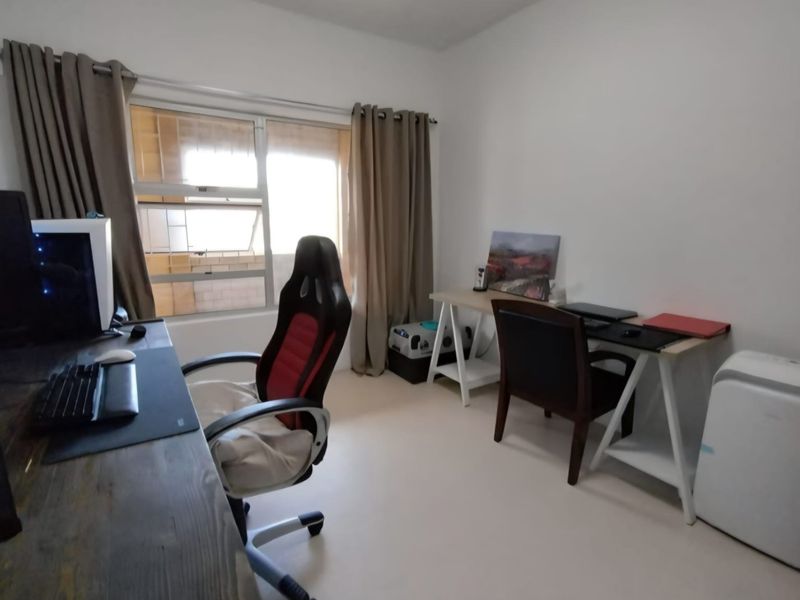 A functional home office space featuring neutral walls and an aluminium-framed window with curtain tracks.