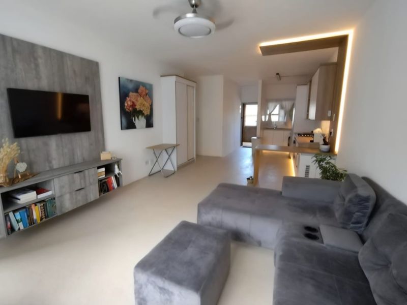 Modern open-plan living area featuring a built-in media console, integrated kitchen cabinetry with breakfast bar, and recessed ceiling lighting.