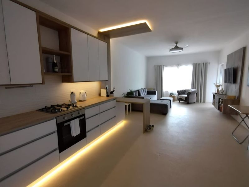 Modern open-plan living area featuring a sleek kitchen with built-in cabinetry, gas hob, oven, and integrated under-cabinet lighting, flowing into a spacious lounge.