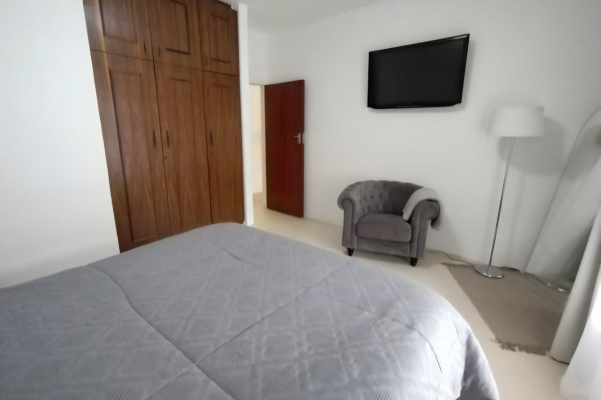 A well-maintained bedroom featuring built-in wooden wardrobes and neutral tiled flooring, providing a clean and functional living space.