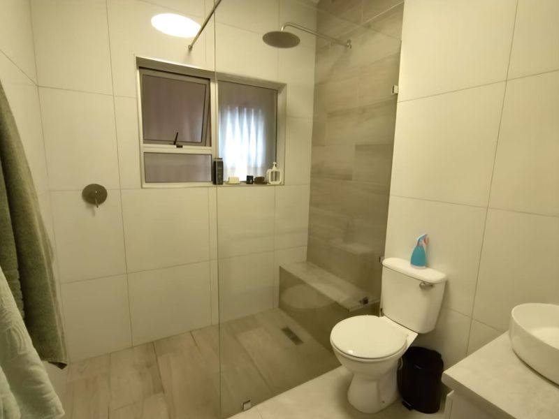 Modern bathroom featuring a walk-in shower with a glass screen, rain shower head, built-in bench, and a contemporary vessel sink.