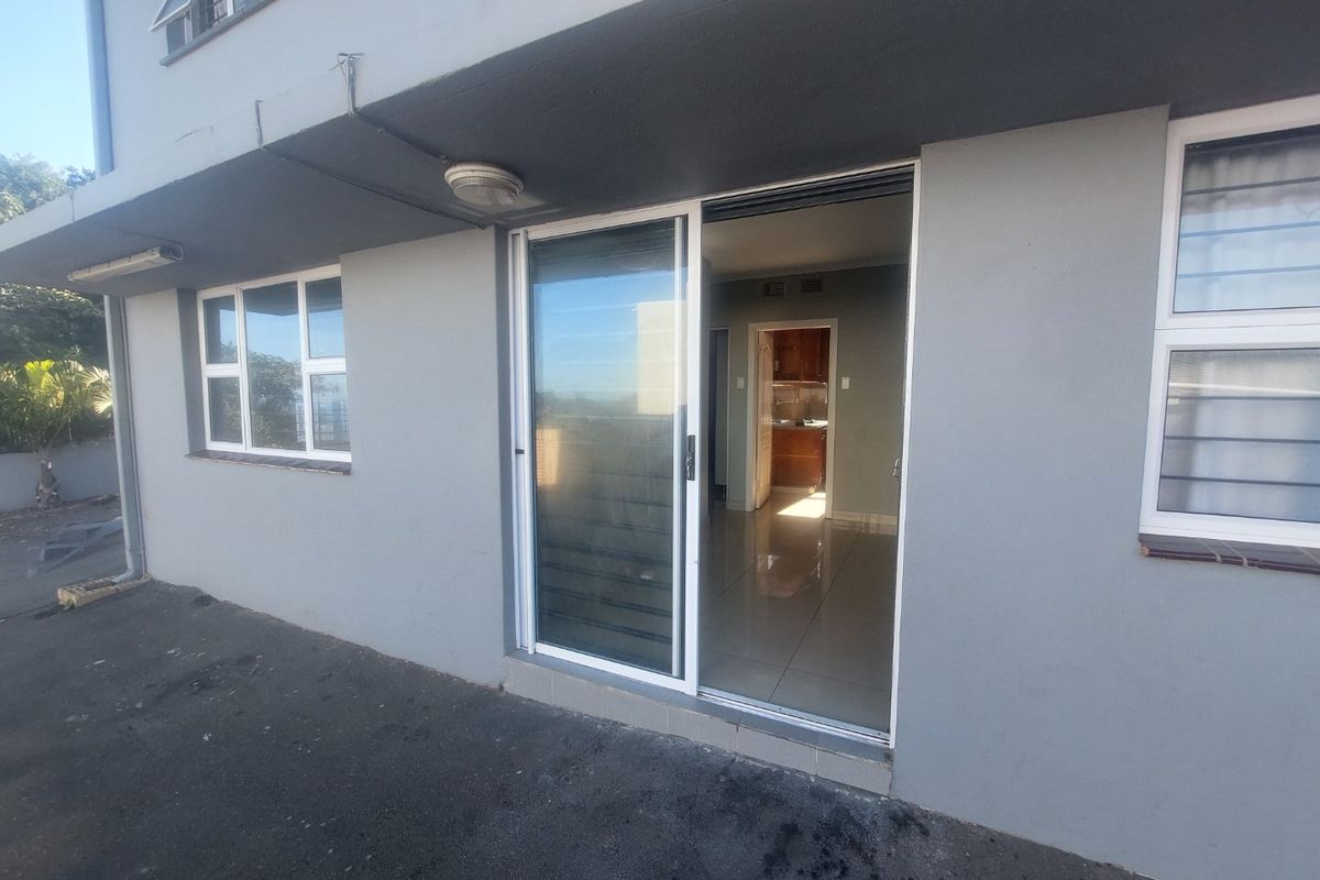 Rear exterior view of the apartment featuring a sliding glass door entrance, aluminium window frames, and paved outdoor area.